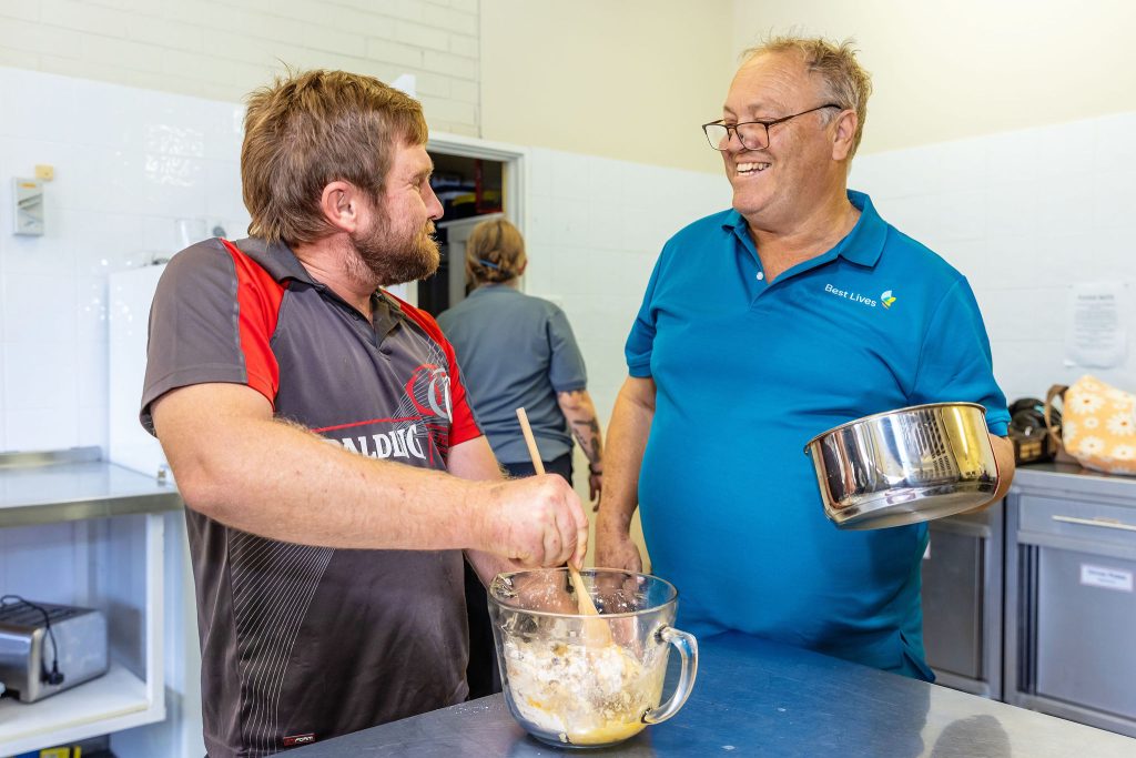 Gentleman preparing food and smiling with a Best Lives support worker